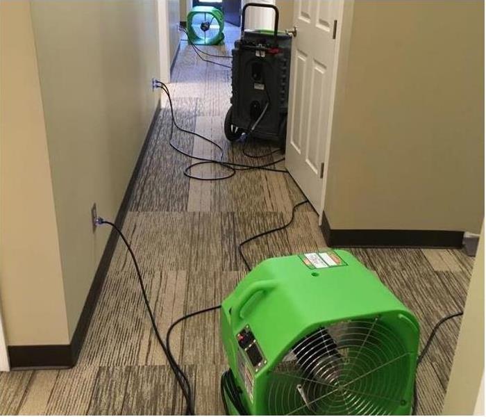 A hallway that has 2 fans and a machine drying the carpet floor 